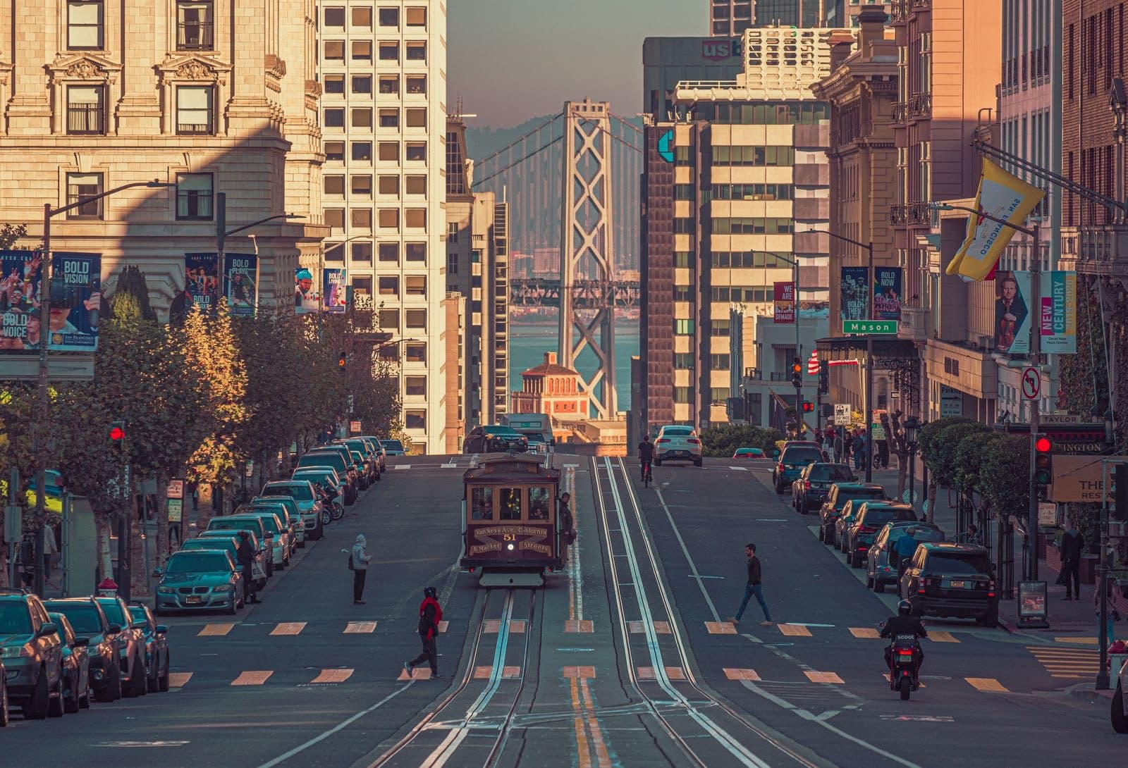 A cable car climbing a downtown San Francisco street toward the Bay Bridge at golden hour
