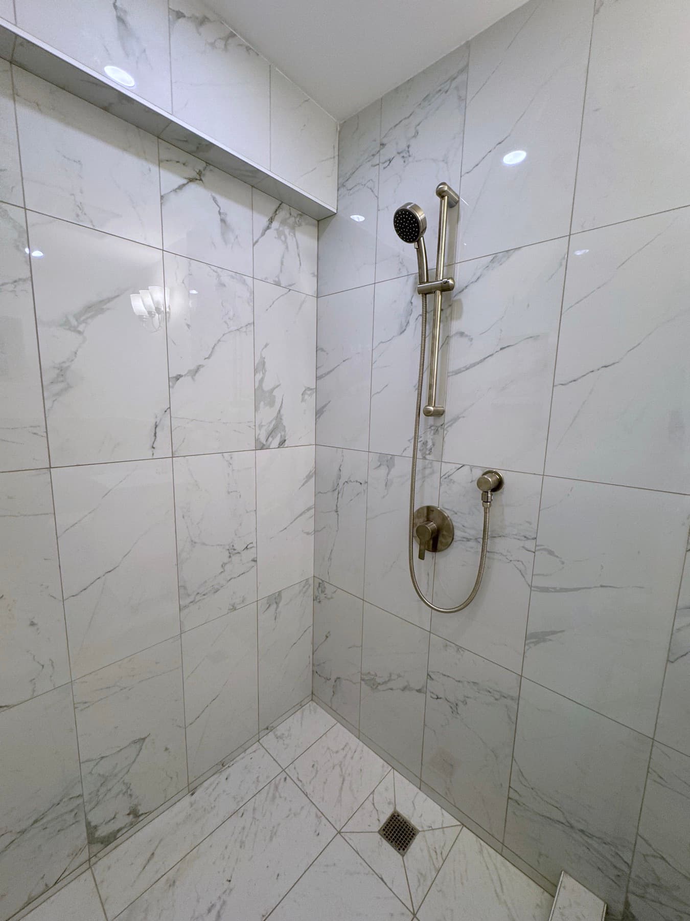 The new bathroom shower, marble-veined tile to the ceiling, a recessed niche along the top, brushed nickel fittings