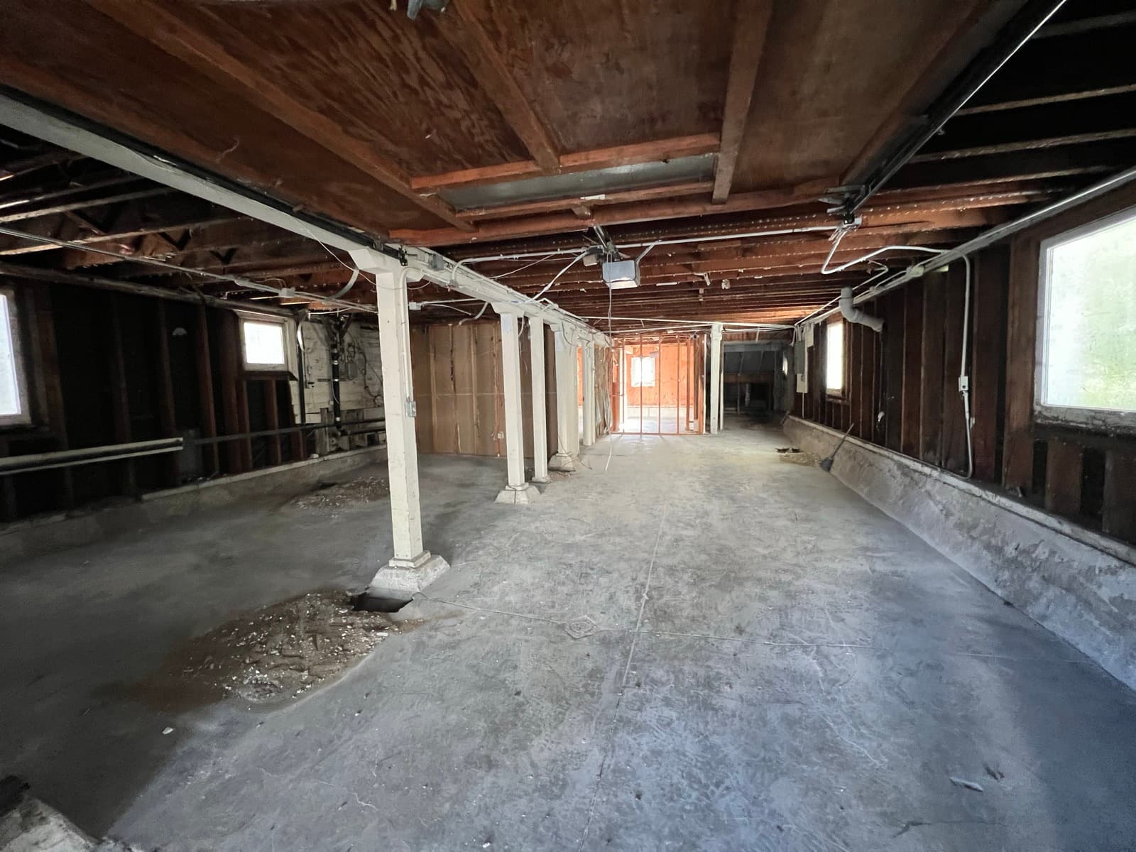 The original garage looking down its length, bare slab, exposed joists overhead, ceilings under seven feet