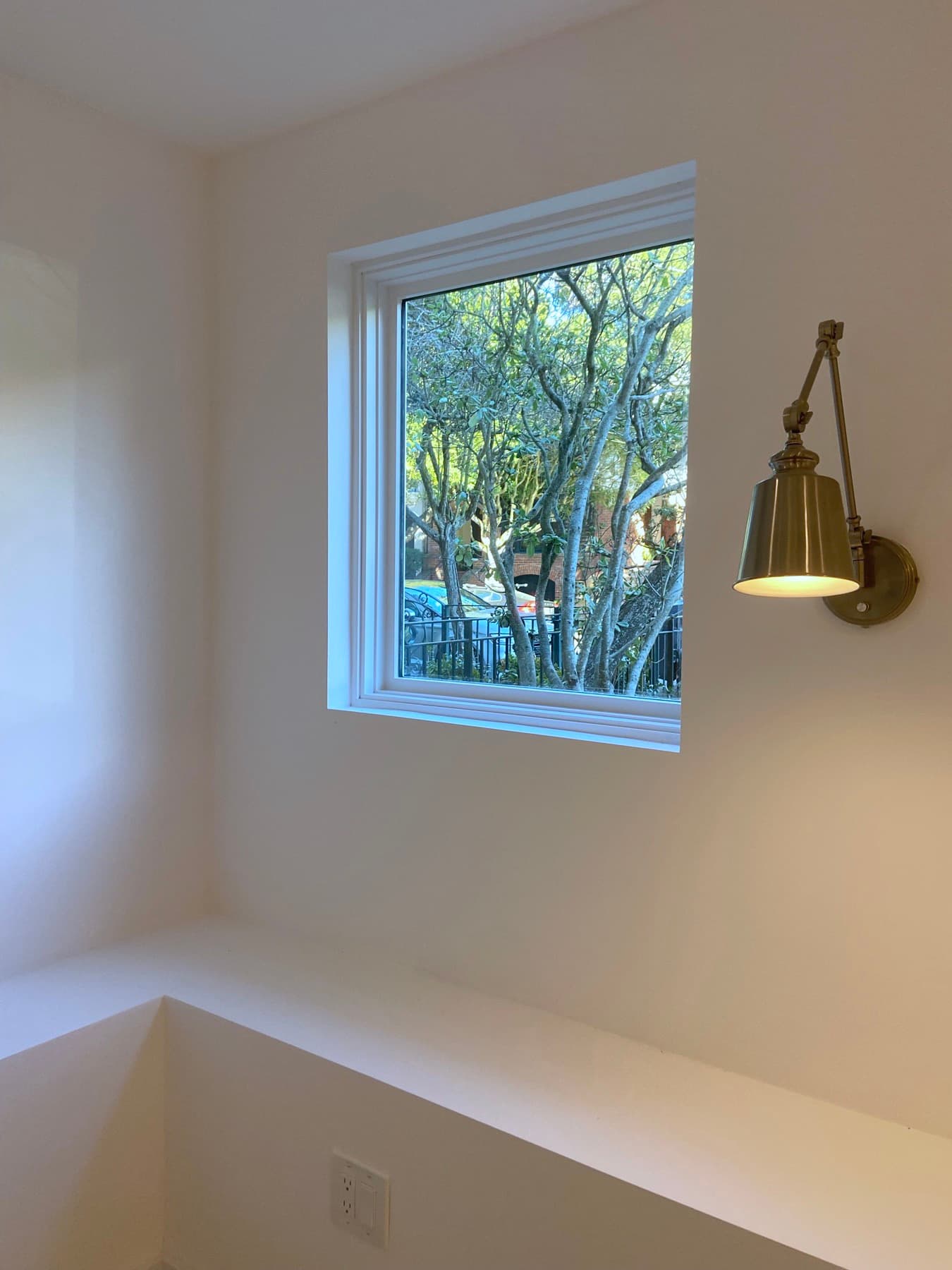 A new window with a brass sconce beside it, the tree outside in full leaf