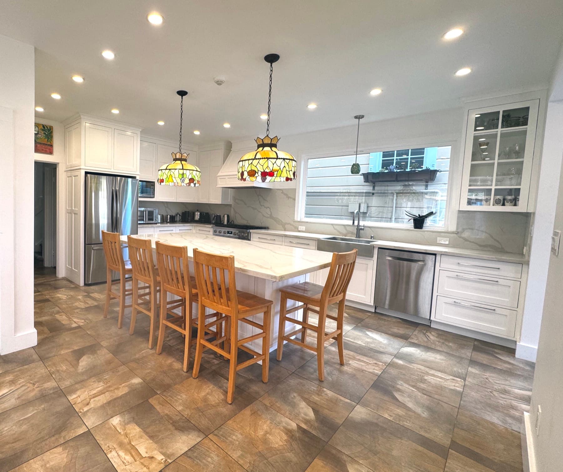 The finished kitchen seen wide: one room, island seating for six, light from both ends